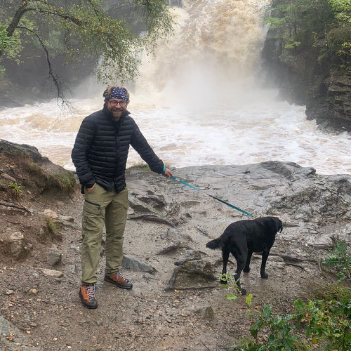 Richard standing at a waterfall with a dog.